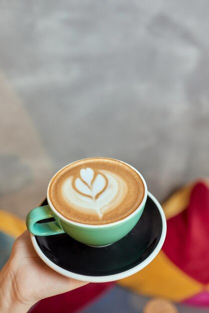 mano sosteniendo cacao orgánico caliente con arte de espuma de espuma en taza de cerámica negra