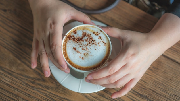 Mano sosteniendo café capuchino caliente