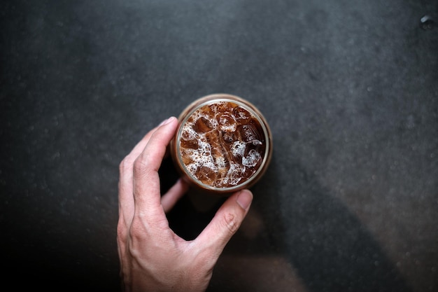 mano sosteniendo un café helado para llevar en una mesa negra