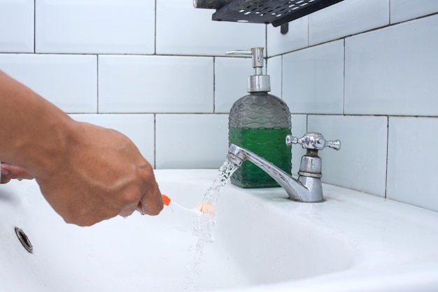 Mano sosteniendo un cepillo de dientes blanco y lávelo con agua corriente del grifo