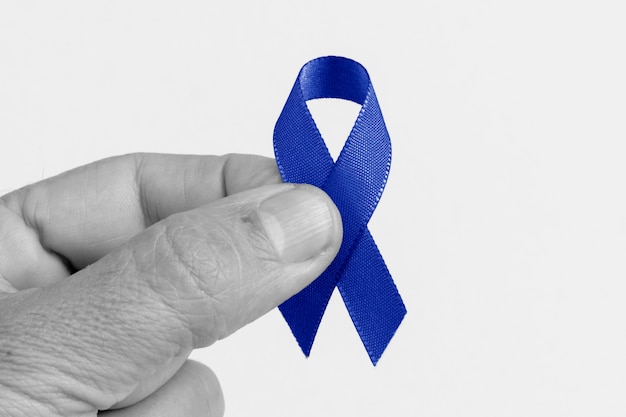 Mano sosteniendo una cinta azul, cáncer colorrectal, conciencia sobre el cáncer de próstata, conciencia sobre la salud de los hombres.