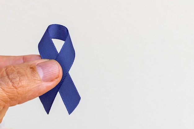 Mano sosteniendo una cinta azul sobre fondo blanco, cáncer colorrectal, conciencia sobre el cáncer de próstata, conciencia sobre la salud de los hombres. Noviembre azul.