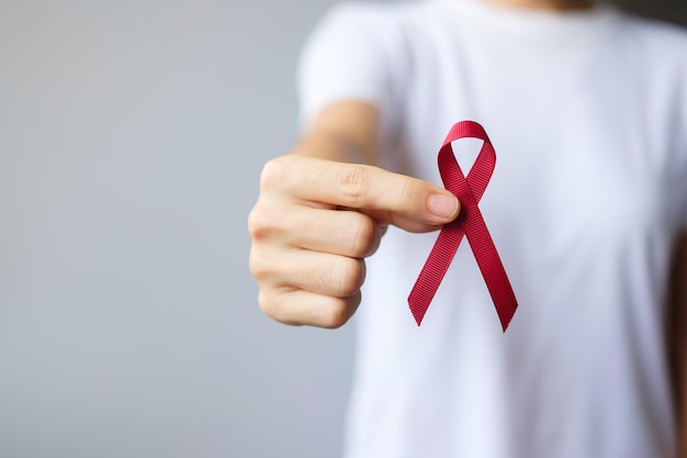 Foto mano sosteniendo la cinta roja de borgoña para el cáncer de mieloma múltiple de marzo y el mes de concientización del día mundial del sida de diciembre. concepto de salud y día mundial del cáncer.