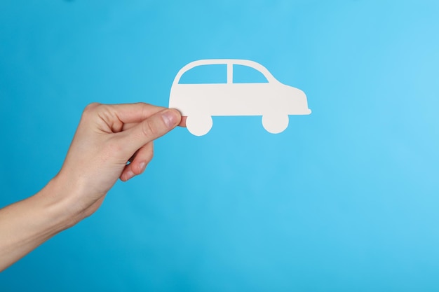 La mano sosteniendo un coche de corte de papel en un fondo azul