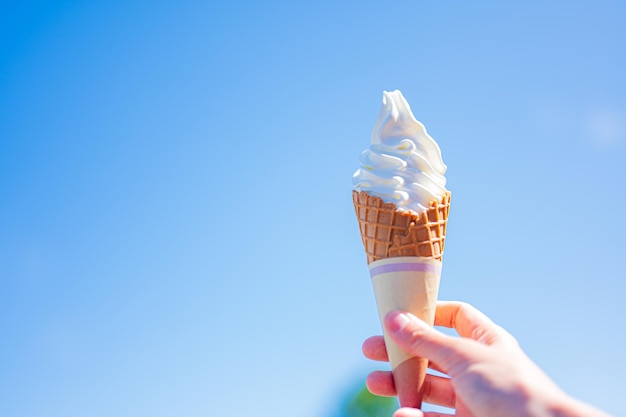 Una mano sosteniendo un cono de galleta con el cielo de fondo