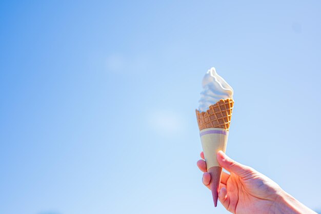 Una mano sosteniendo un cono de helado contra un cielo azul.