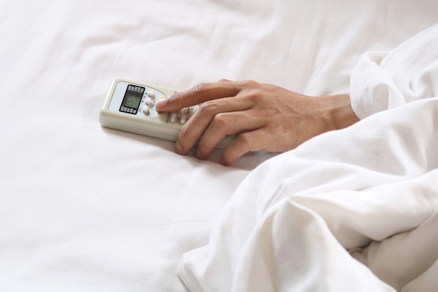 mano sosteniendo el control remoto de aire acondicionado en la cama