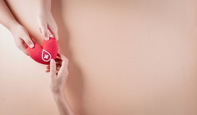 Mano sosteniendo un corazón rojo hecho a mano con un signo o símbolo de donación de sangre