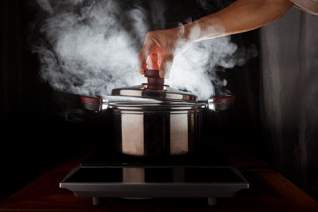 Foto mano sosteniendo la cubierta de olla de metal con vapor caliente que fluye desde el interior