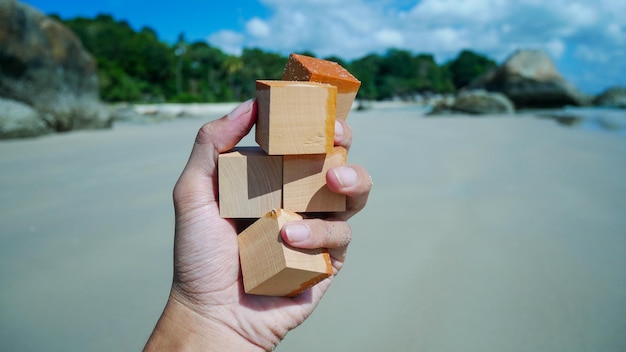 Mano sosteniendo cubos de madera de maqueta con el fondo de la playa Cubos de madera de espacio libre para su texto