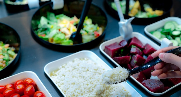 Mano sosteniendo una cuchara con lágrimas de Job hervidas en la barra de ensaladas. Buffet de ensaladas en el restaurante. Buffet de ensaladas frescas para el almuerzo o la cena. Comida sana. Catering comida. Servicio de banquetes. Comida vegetariana.