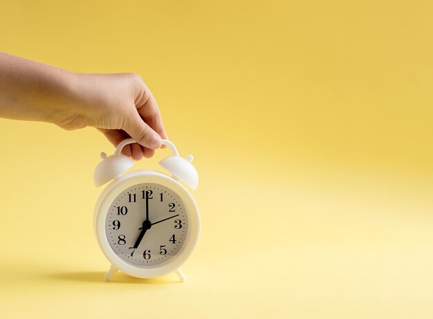 Mano sosteniendo un despertador blanco Fondo amarillo Concepto de tiempo Copia espacio