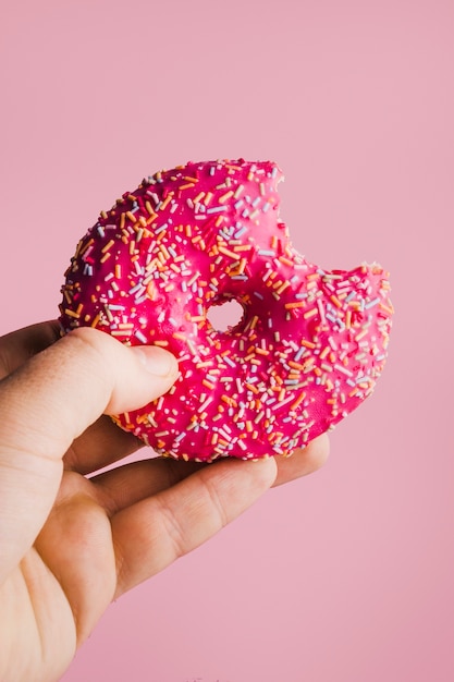 Mano sosteniendo donut glaseado rosa