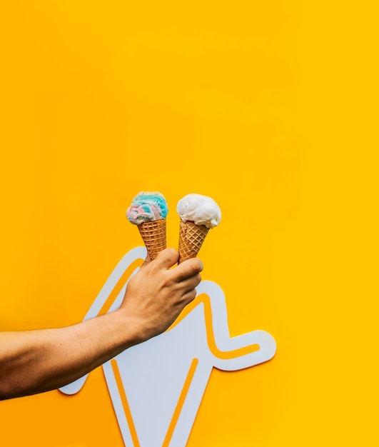 Mano sosteniendo dos helados de cono de galleta aislado Mano sosteniendo dos cono de helado sobre fondo amarillo Concepto de helado de cono de galleta sobre fondo amarillo