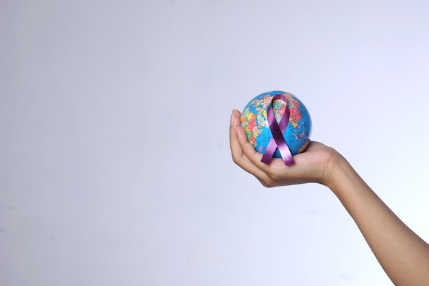 Mano sosteniendo un globo terráqueo con cinta morada para el concepto del Día Mundial contra el Cáncer