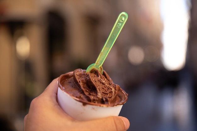 Mano sosteniendo un helado de chocolate en una tina en las calles de Roma.