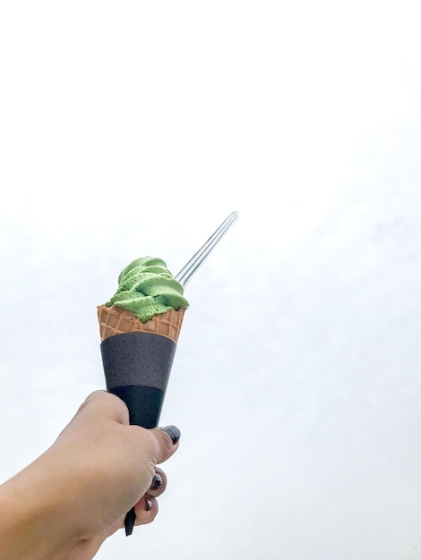 Mano sosteniendo helado de matcha de té verde en el cono con una cuchara de plástico transparente