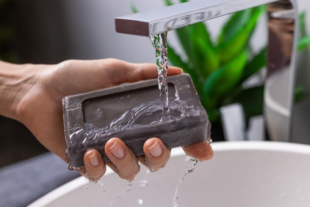 Mano sosteniendo jabón cerca del fregadero con agua