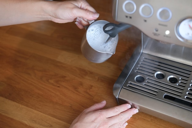 Mano sosteniendo la jarra de leche y haciendo espuma para café capuchino