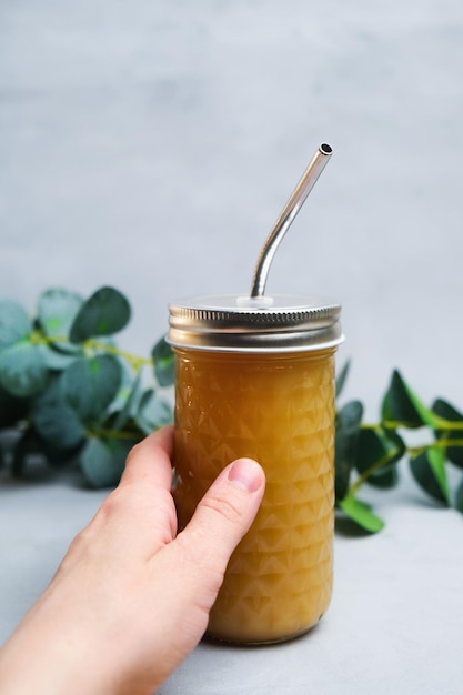 Mano sosteniendo jugo de fruta en vidrio reutilizable con pajita de metal