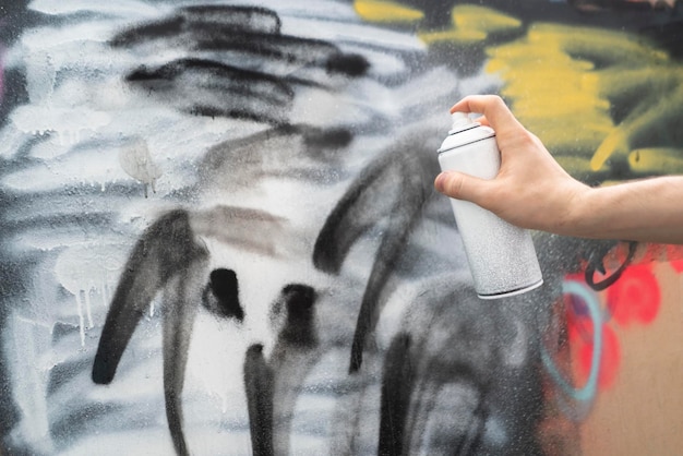 Una mano sosteniendo una lata de pintura en aerosol haciendo arte de graffiti en la pared