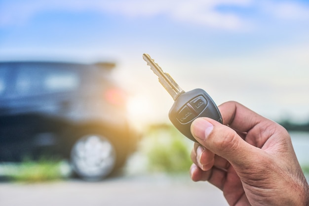 Mano sosteniendo la llave y el automóvil estacionado en la carretera