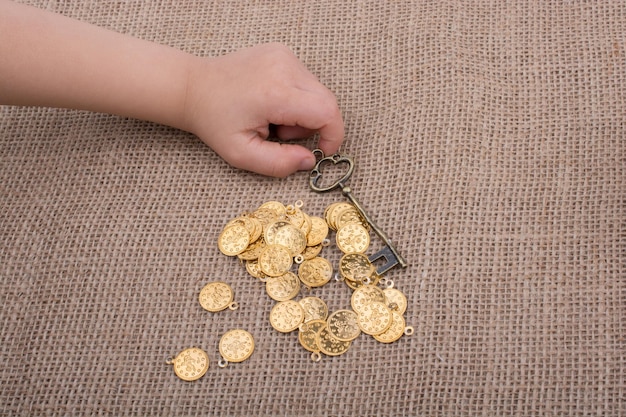 Mano sosteniendo una llave de estilo retro sobre monedas de oro falsas