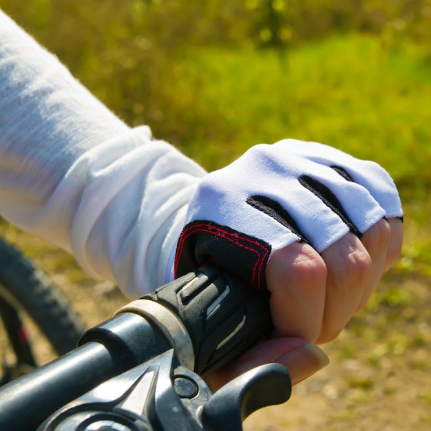 Mano sosteniendo un manillar. Mujer montando una bicicleta en un parque