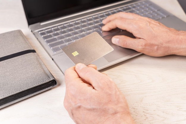 Mano sosteniendo maqueta de tarjeta de crédito bancaria maqueta de tarjeta bancaria con chip en el lugar de trabajo ingresando datos para pago en línea con teclado de computadora portátil