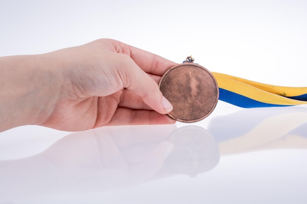 Mano sosteniendo una medalla con cinta azul y amarilla