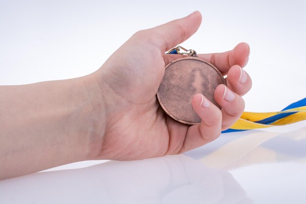 Mano sosteniendo una medalla con cinta azul y amarilla