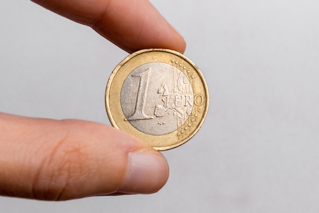 Mano sosteniendo una moneda de euro en primer plano de fondo blanco.