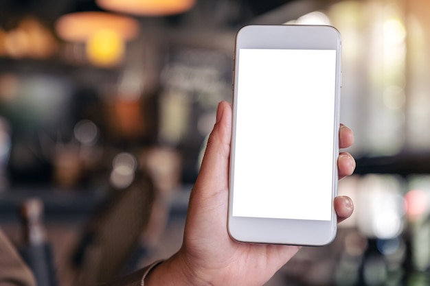 Mano sosteniendo y mostrando un teléfono móvil blanco con pantalla en blanco en el café