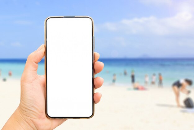 Mano sosteniendo una pantalla en blanco del teléfono en la playa