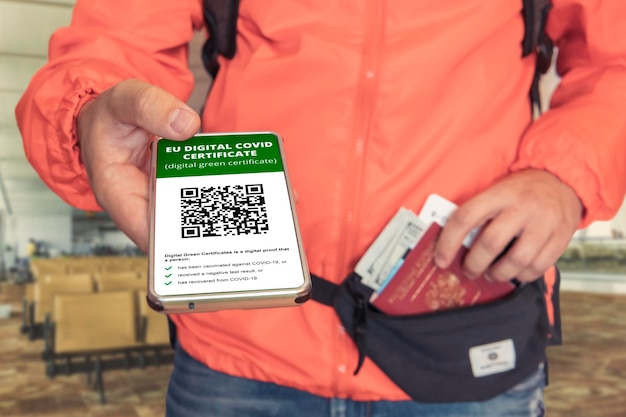 Foto mano sosteniendo la pantalla del teléfono inteligente en la aplicación móvil vacunado covid19 o certificado covipass pasaporte de vacuna de inmunidad en el mostrador de facturación del aeropuerto el hombre muestra un certificado de vacunación electrónico