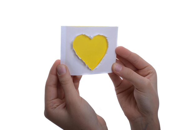 Mano sosteniendo un papel con forma de corazón amarillo cortado de papel sobre un fondo blanco