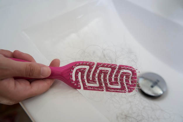 Foto mano sosteniendo un peine rosa con pelos enredados debido a un problema de pérdida de cabello en un lavabo
