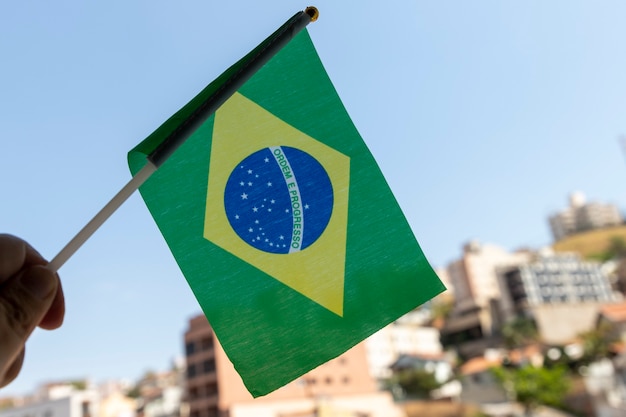 Mano sosteniendo la pequeña bandera de Brasil. Orden y progreso en portugués. Bandera brasileña