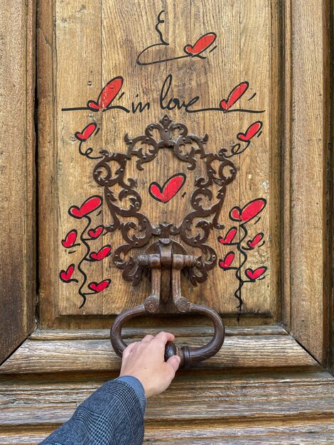 Foto mano sosteniendo la perilla de la puerta en la puerta de madera con corazones persona