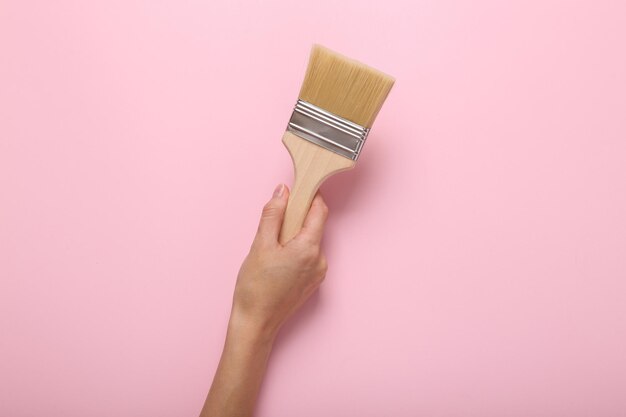 La mano sosteniendo un pincel de pintura sobre un fondo rosado