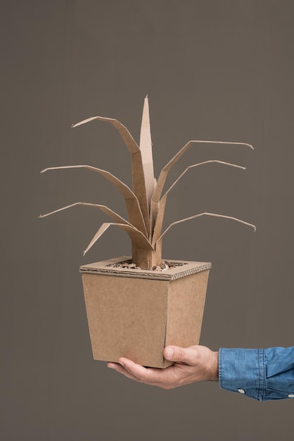 Mano sosteniendo una planta decorativa hecha de cartón reciclado, artesanía y concepto de creatividad.