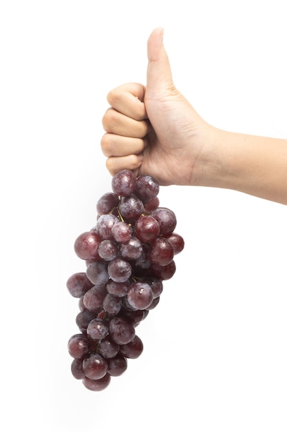 Mano sosteniendo un racimo de uvas rojas frescas con el dedo pulgar aislado sobre fondo blanco.