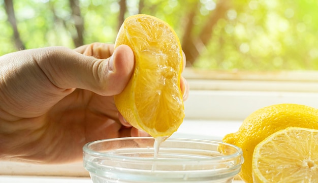 Mano sosteniendo una rodaja de limón y exprimiendo el jugo fresco en los tazones