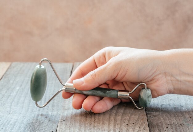 Mano sosteniendo un rodillo de masaje guasha verde jade utilizado para masaje facial