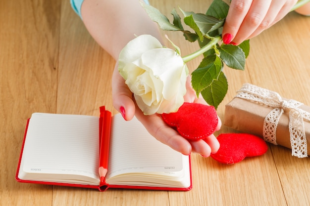 Mano sosteniendo una rosa blanca en cuaderno abierto y corazones