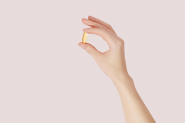 Mano sosteniendo los suplementos de vitaminas omega 3 sobre fondo rosa