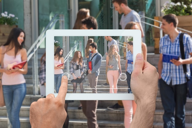 Foto mano sosteniendo tablet pc contra estudiantes felices caminando y charlando afuera