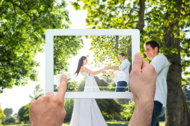 Mano sosteniendo tablet pc mostrando pareja feliz en el parque