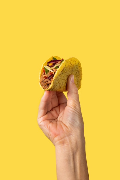 Foto mano sosteniendo un taco mexicano sobre fondo amarillo