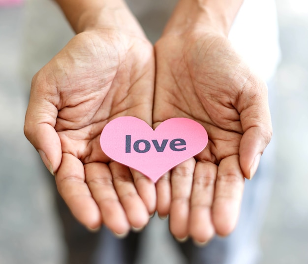 Mano sosteniendo la tarjeta de corazón rosa